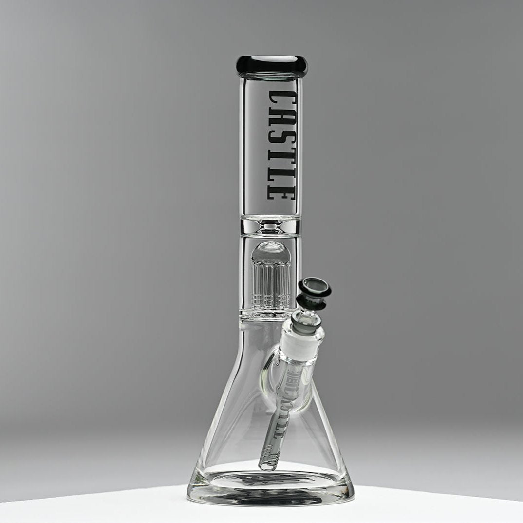 A glass beaker bong with the "Castle" logo prominently displayed on the neck, featuring an 8-arm percolator inside. The bong is set against a minimalist grey background, emphasizing its clean lines and modern design. The photo captures the bong from the right side, highlighting its structure and details.