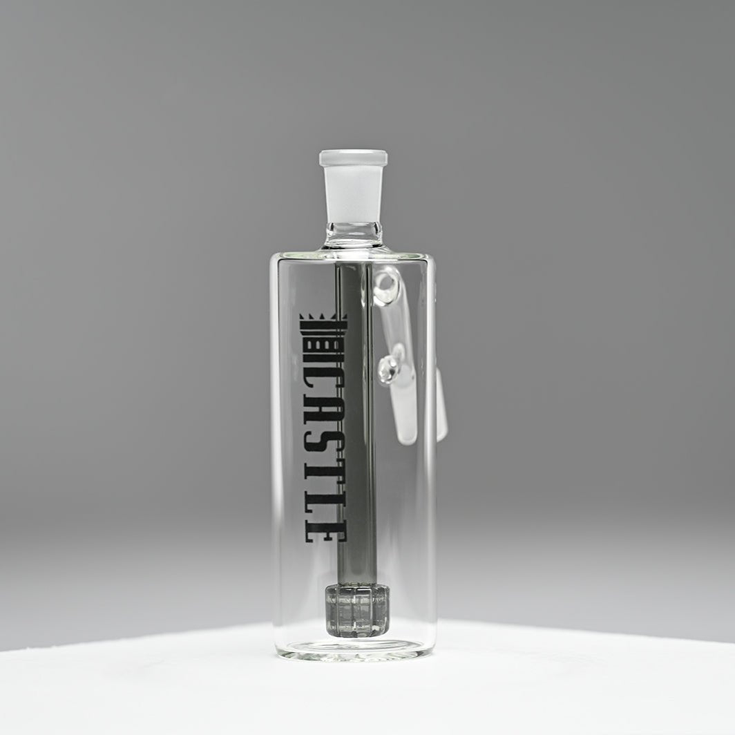 A glass ash catcher with a sleek, minimalist design, featuring the brand name Castle in bold black letters on the side. The ash catcher is equipped with a black matrix percolator. It is set against a smooth, grey background that highlights the clean lines and transparency of the glass. The image emphasizes the modern and sophisticated look of the ash catcher, with the branding and design elements standing out clearly.