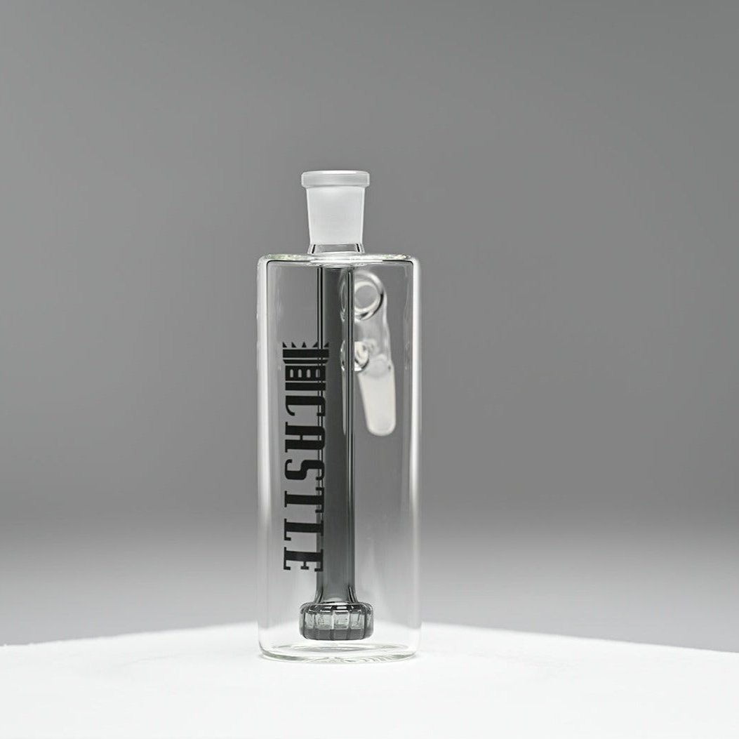 A clear glass ash catcher featuring the brand name "CASTLE" in bold black letters on the side, with a matching black showerhead percolator. The ash catcher is positioned against a neutral grey background, which highlights the sleek and modern design of the piece. The transparent glass and clean lines are prominently displayed, emphasizing the minimalist and sophisticated craftsmanship.