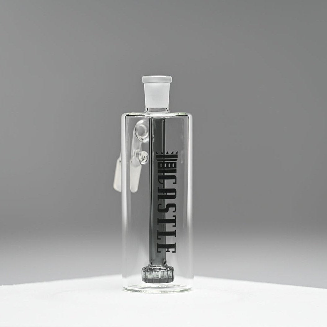 A clear glass ash catcher featuring the brand name "CASTLE" in bold black letters on the side, with a black showerhead percolator. The ash catcher is positioned against a neutral grey background, which enhances the sleek and modern design of the piece. The transparent glass and precise craftsmanship are highlighted, giving the ash catcher a minimalist and sophisticated appearance.