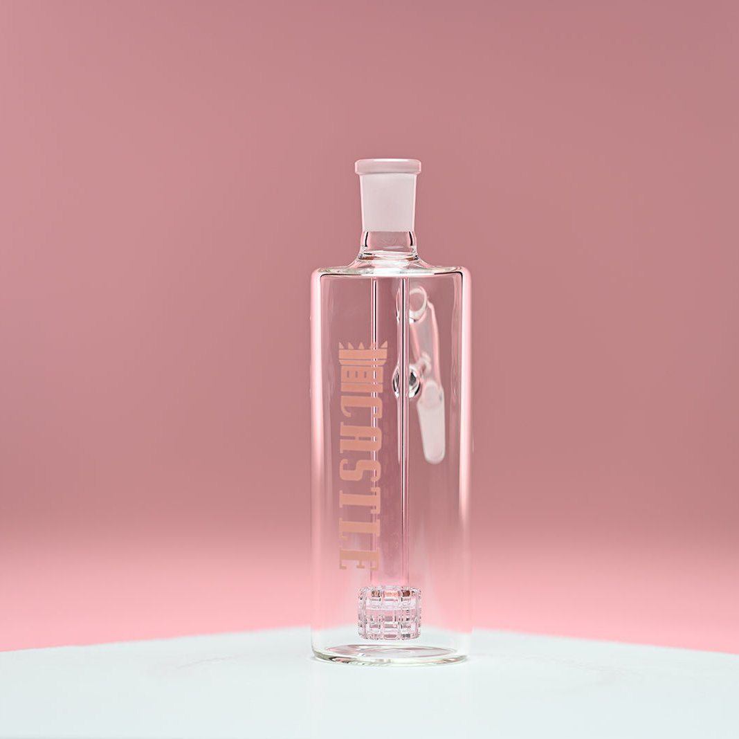 A glass ash catcher featuring the brand name Castle in soft pink letters on the side, with a matching pink matrix percolator. The ash catcher is set against a smooth pink background, which complements the delicate pink color of the percolator and branding. The transparent glass design and clean lines are prominently displayed, highlighting the elegant and modern craftsmanship of the piece.iece.